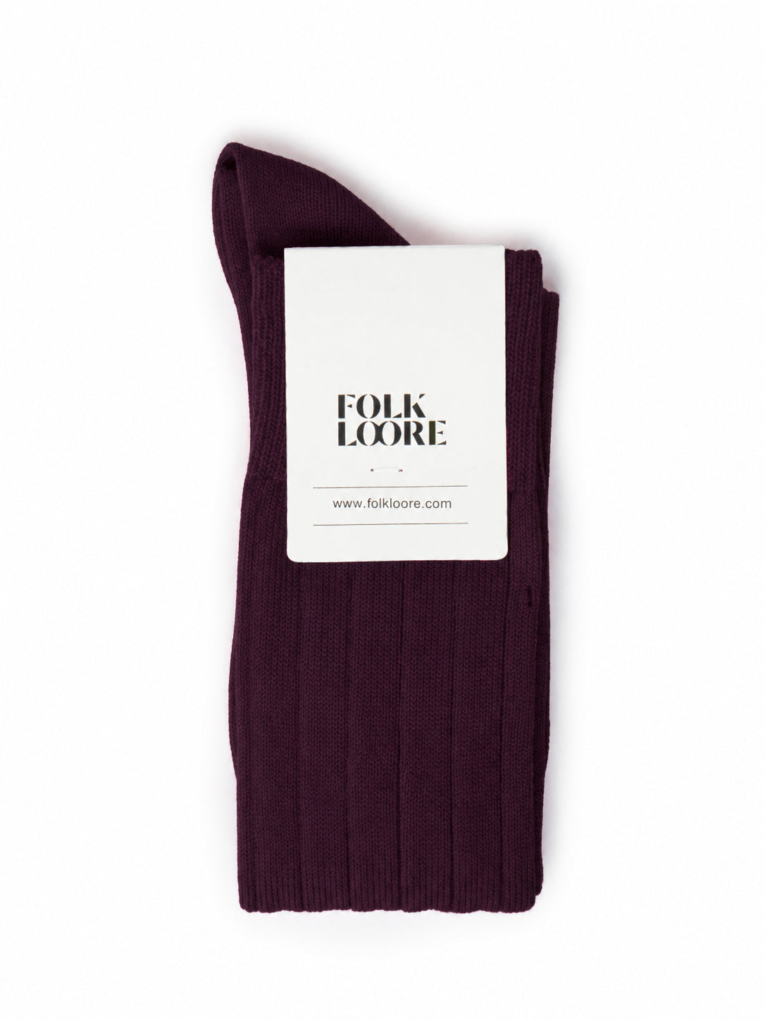 A single dark plum purple ribbed knit sock folded with a white paper tag that reads 'FOLK LOORE' on a plain white background. socks, cotton socks, high-knee socks, made in italy, handmade, artigianally made, fatto a mano, calzettoni invernali, winter cotton, calze di cotone, calze di cachemire, cachemire socks, cashmire socks