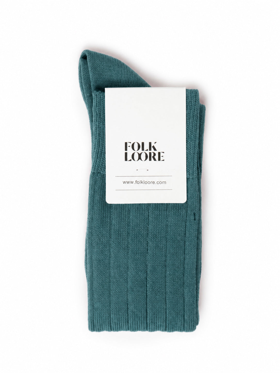 A single folded ribbed knit sock in teal blue-green, with a white paper label attached that reads 'FOLK LOORE' and 'www.folkloore. socks, cotton socks, high-knee socks, made in italy, handmade, artigianally made, fatto a mano, calzettoni invernali, winter cotton, calze di cotone, calze di cachemire, cachemire socks, cashmire socks