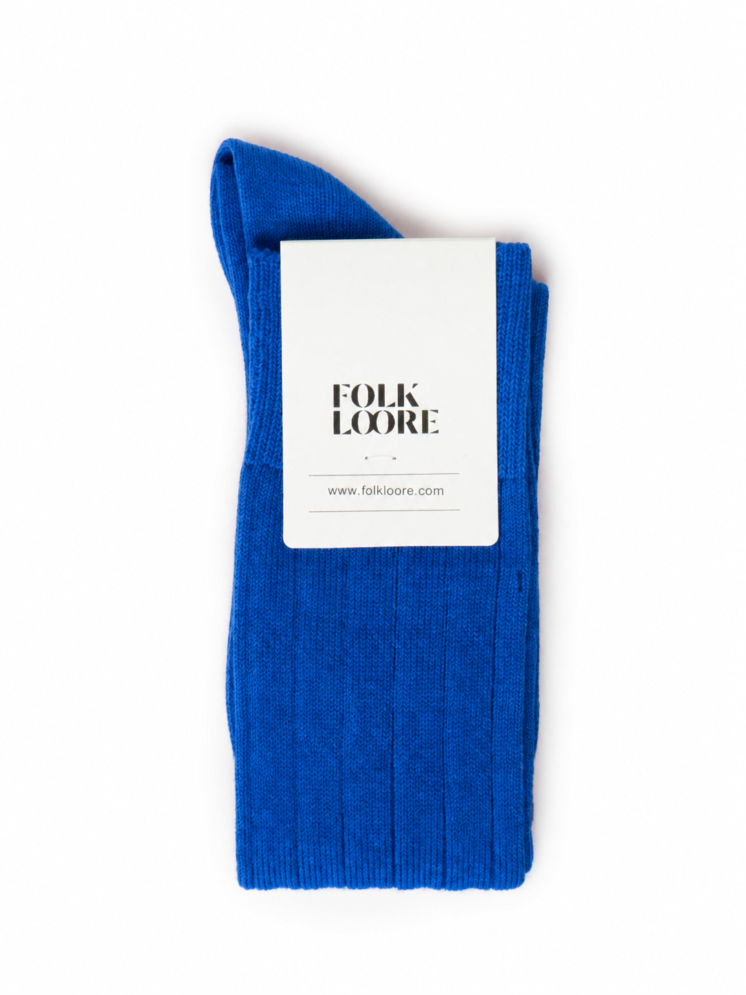 A single royal blue ribbed knit sock folded with a white paper label that reads 'FOLK LOORE' and a website, photographed on a plain white background. socks, cotton socks, high-knee socks, made in italy, handmade, artigianally made, fatto a mano, calzettoni invernali, winter cotton, calze di cotone, calze di cachemire, cachemire socks, cashmire socks
