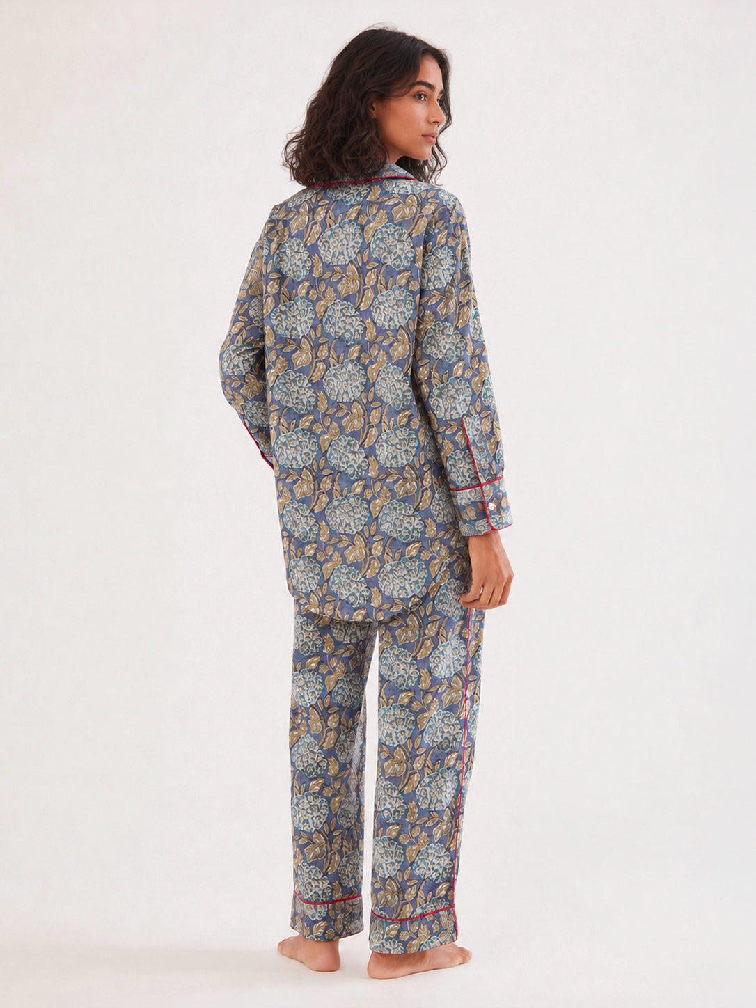 A woman modeling a matching two-piece pajama set with a blue, beige, and white floral pattern, shown from the back against a plain white studio background. ETHICAL FASHION, CRAFTSMANSHIP, SUSTAINABLE FASHION, TRADITIONAL FASHION, ETHNIC FASHION, BOHEMIAN FASHION, MODA ETICA, MODA SOSTENIBILE, TECNICHE ARTIGIANALI, MODA TRADIZIONALE, MODA ETNICA, BOHEMIAN DRESS, MADE IN INDIA, HANDMADE IN INDIA, BLOCK PRINT, FLOWER PAJAMAS, PIGIAMA A FIORI, PIGIAMA DI COTONE, COTTON PAJAMA, SILK PAJAMA, PIGIAMA DI SETA, VEST