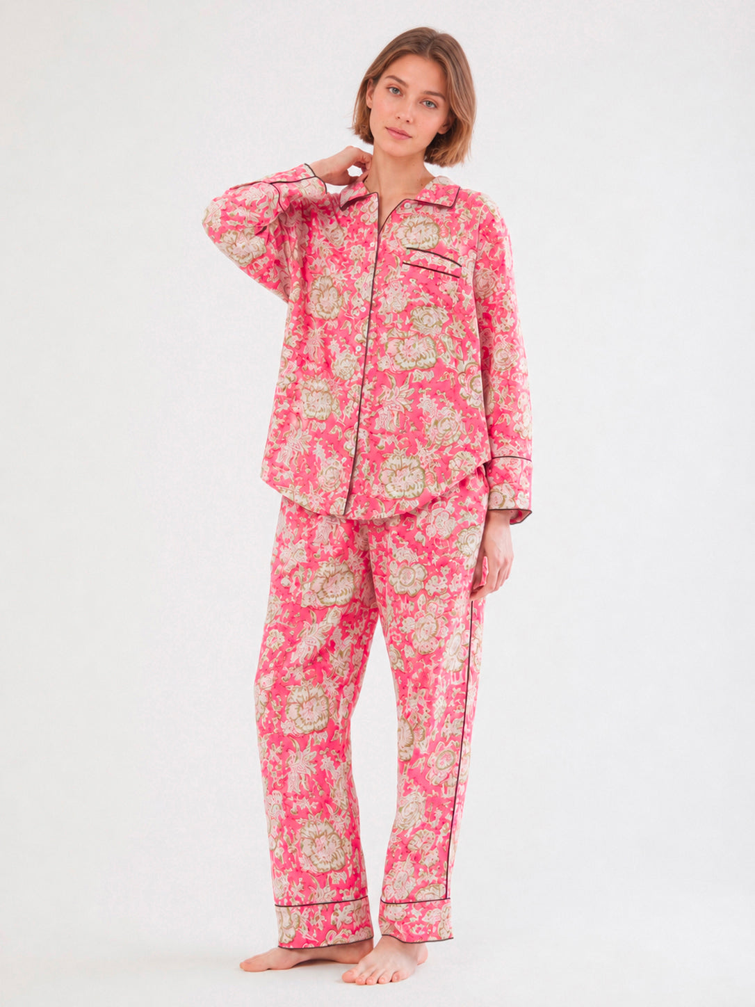 A woman modeling a two-piece pajama set with a pink and beige floral pattern, standing against a plain white studio background. ETHICAL FASHION, CRAFTSMANSHIP, SUSTAINABLE FASHION, TRADITIONAL FASHION, ETHNIC FASHION, BOHEMIAN FASHION, MODA ETICA, MODA SOSTENIBILE, TECNICHE ARTIGIANALI, MODA TRADIZIONALE, MODA ETNICA, BOHEMIAN DRESS, MADE IN INDIA, HANDMADE IN INDIA, BLOCK PRINT, FLOWER PAJAMAS, PIGIAMA A FIORI, PIGIAMA DI COTONE, COTTON PAJAMA, SILK PAJAMA, PIGIAMA DI SETA, VESTAGLIA, NIGHTWEAR, SLEEPWEAR,