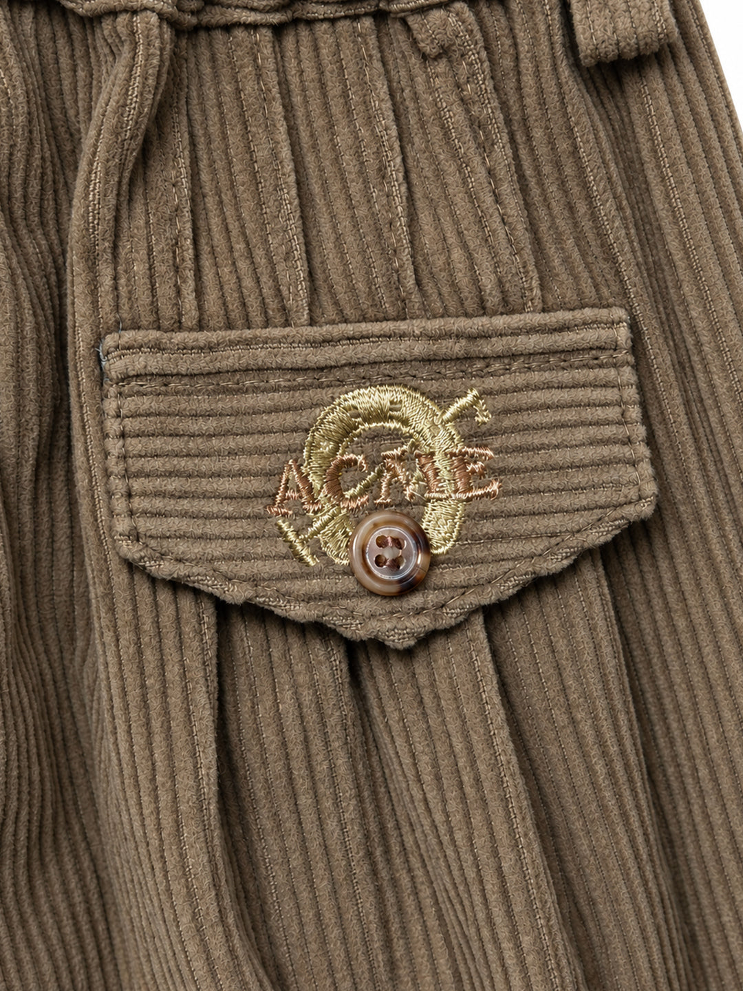 Close-up of a brown corduroy garment featuring a front pocket with a flap and a decorative metallic gold embroidered logo patch with a brown button. Argentine Bombacha Pants, horseback riding, traditional gaucho, Argentine cowboy attire. Soft and breathable fabrics, perfect pants for all-day wear. With a loose fit and elasticated waistband, they allow for plenty of movement, while the high waist provides extra coverage. Everyday look, perfect for both urban and countryside adventures. Cotton Corduroy, KIDS,