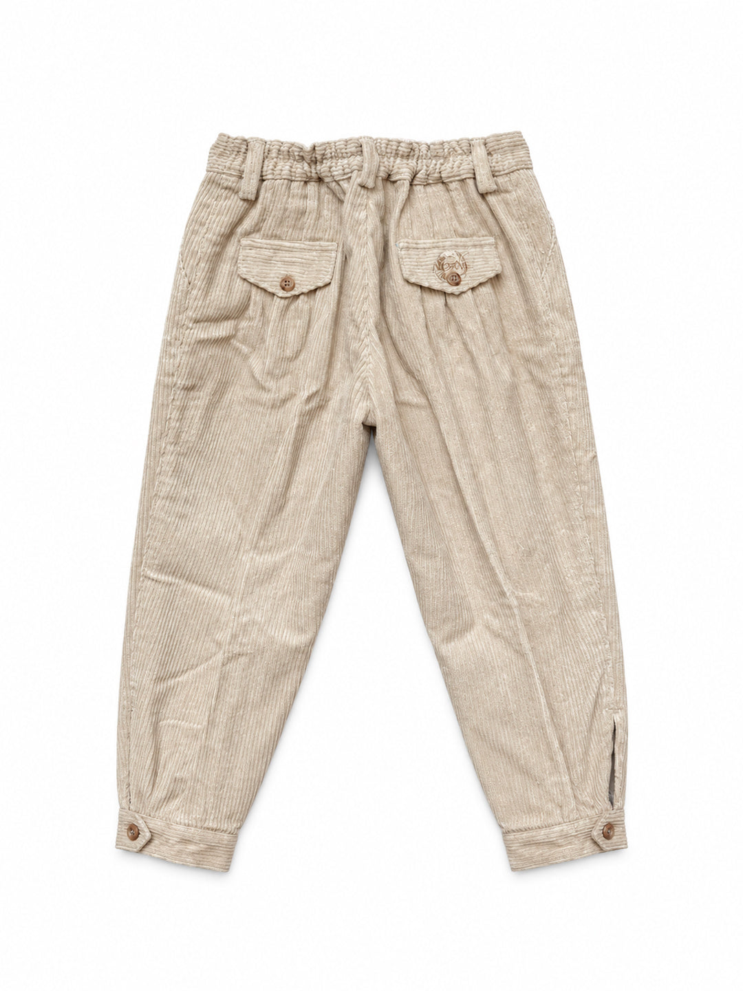 A pair of beige corduroy trousers for children, featuring an elastic waistband, two front flap pockets with decorative button details, and buttoned cuffs at the ankles, shown flat on a white background. Argentine Bombacha Pants, horseback riding, traditional gaucho, Argentine cowboy attire. Soft and breathable fabrics, perfect pants for all-day wear. With a loose fit and elasticated waistband, they allow for plenty of movement, while the high waist provides extra coverage. Everyday look, perfect for both ur